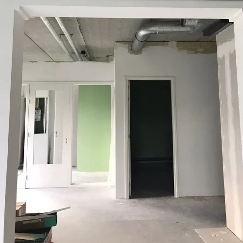Afbouwfase met witte deuren en kozijnen, groene wand en leidingwerk in het plafond