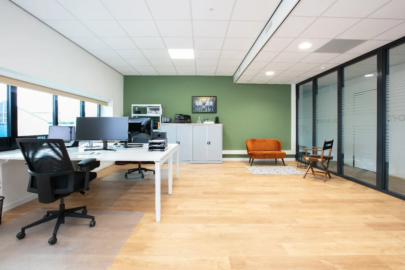 Ingericht huurderskantoor met groene accentwand, witte bureaus en een glazen wand