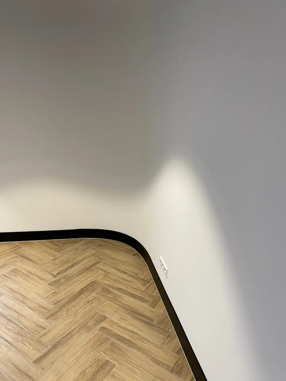 Ronde binnenhoek met meebuigende zwarte plint op een visgraatvloer